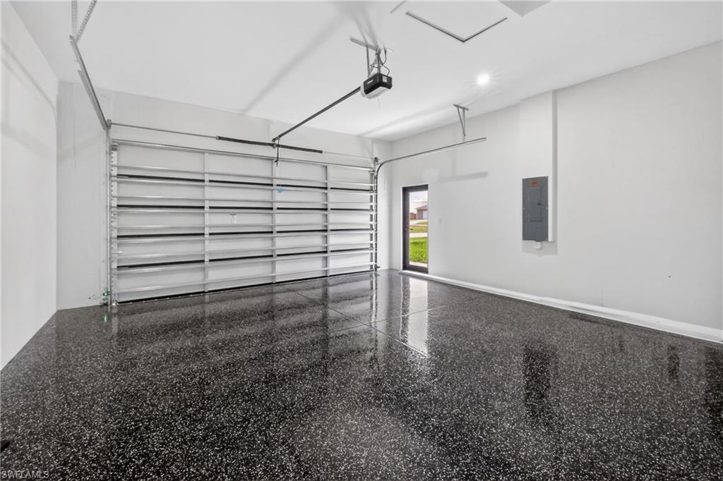 Spacious garage featuring a durable epoxy speckled flooring, an automatic garage door opener, a side entry door, recessed lighting, and a visible electrical panel