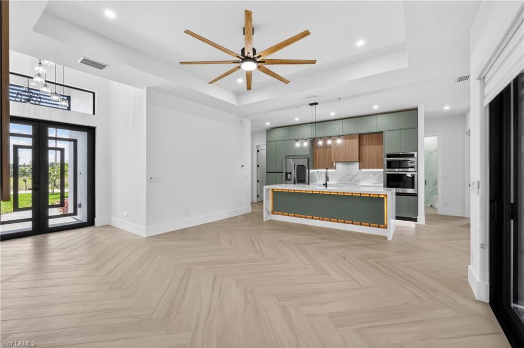 Open-concept living space featuring light wood-finish flooring in a herringbone pattern, a contemporary kitchen island with a quartz countertop, modern cabinetry, and recessed lighting