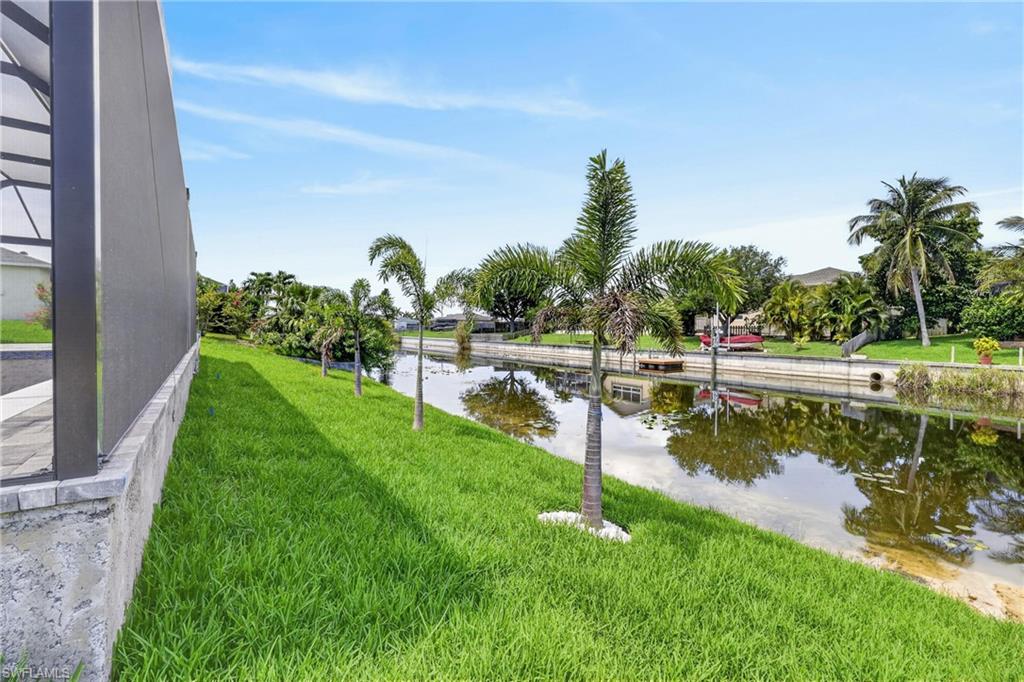 Waterfront property featuring a screened enclosure, lush lawn, palm trees, and canal access