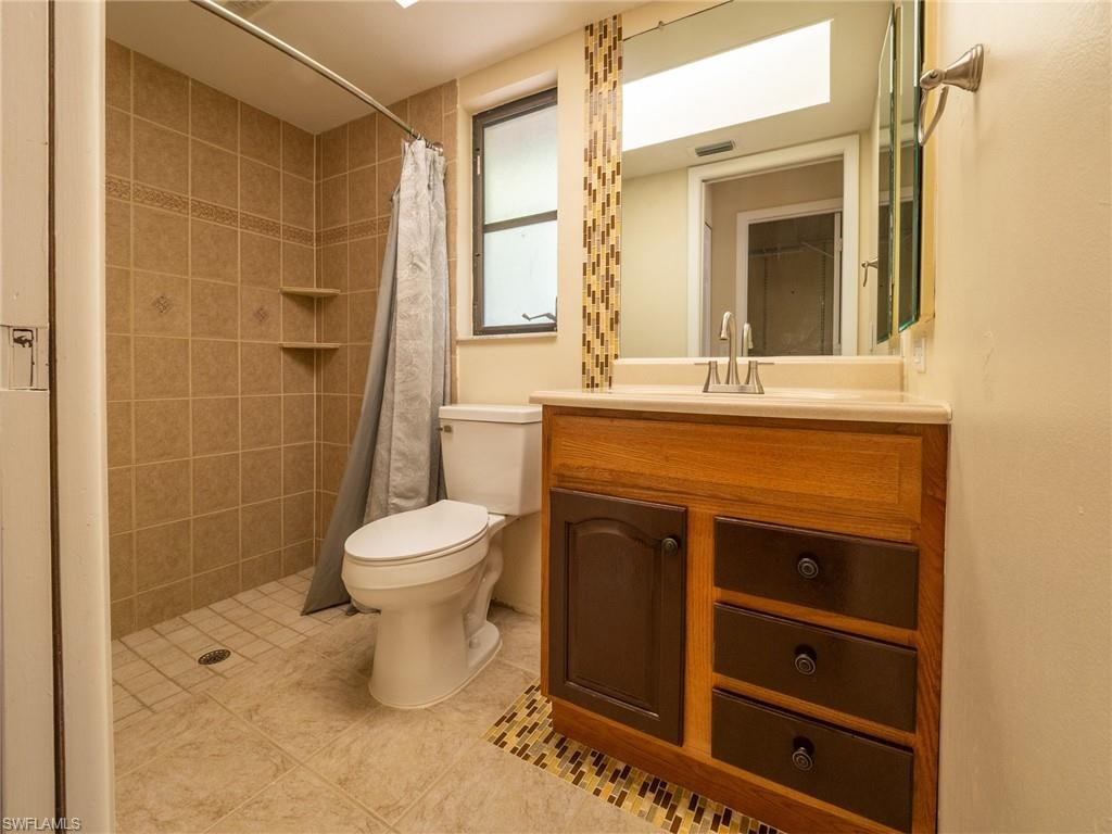 Bathroom featuring a walk-in shower with tile surround, a single vanity with a light wood-tone cabinet and contrasting drawer fronts, a solid surface countertop, and a built-in window