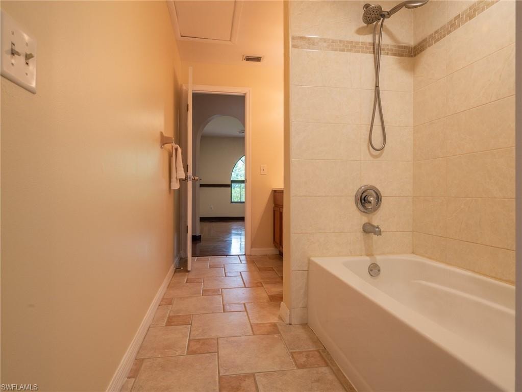 Bathtub and shower combination featuring a tiled surround with decorative accent band