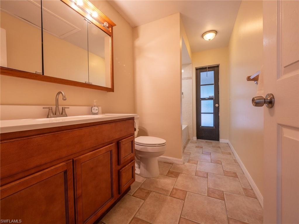 Bathroom featuring a wood-finish vanity with an integrated sink and brushed nickel faucet, a medicine cabinet with integrated lighting, a toilet, and tiled flooring
