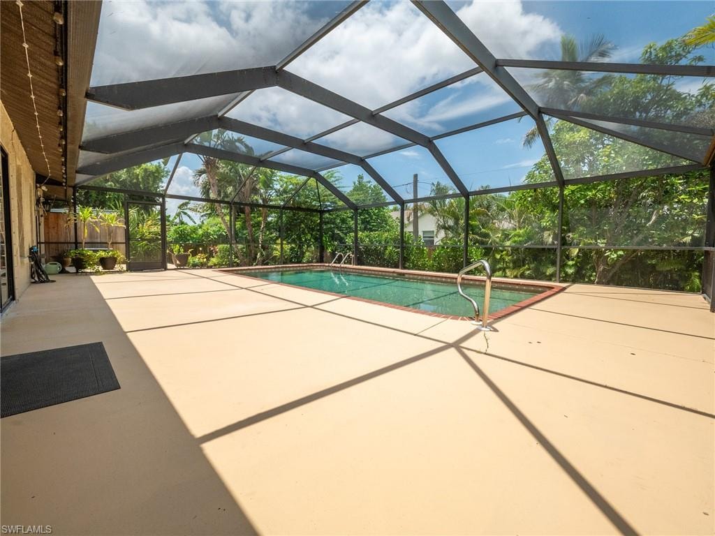 Screened pool enclosure featuring a rectangular swimming pool with brick coping, a large concrete deck, and perimeter landscaping