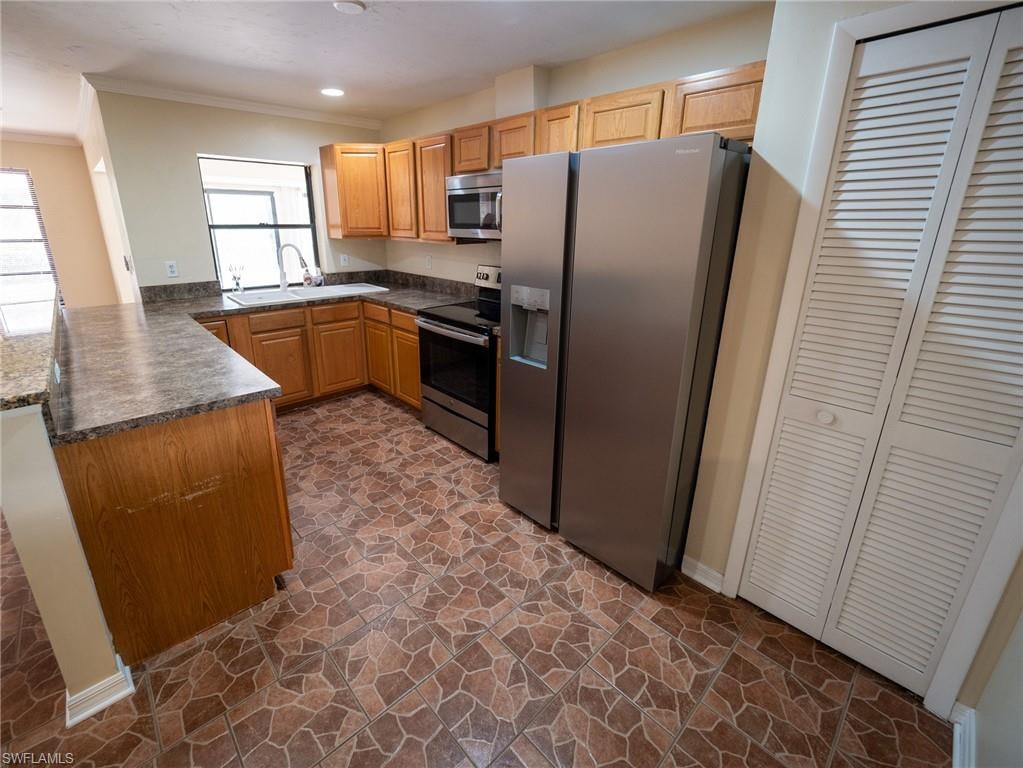Kitchen featuring L-shaped wood cabinetry with coordinating countertops, stainless steel appliances, a double basin sink under a window, and patterned tile flooring
