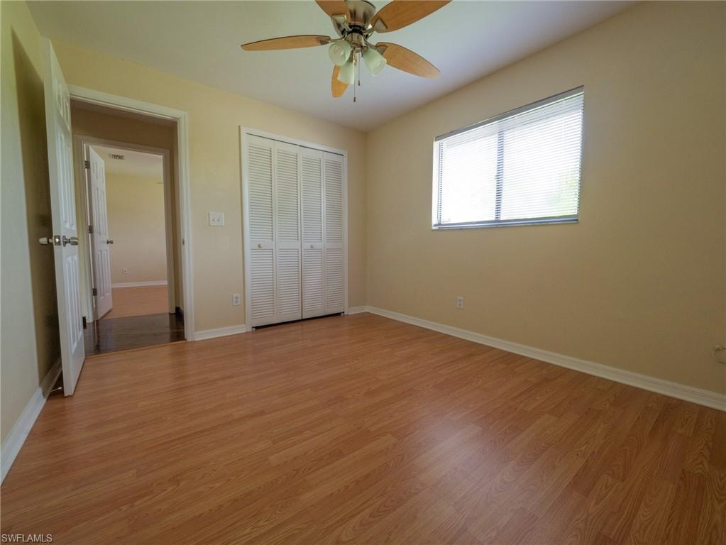 Room featuring wood-finish flooring, a ceiling fan with light fixture, louvered bi-fold closet doors, a window with blinds, and light-toned wall paint
