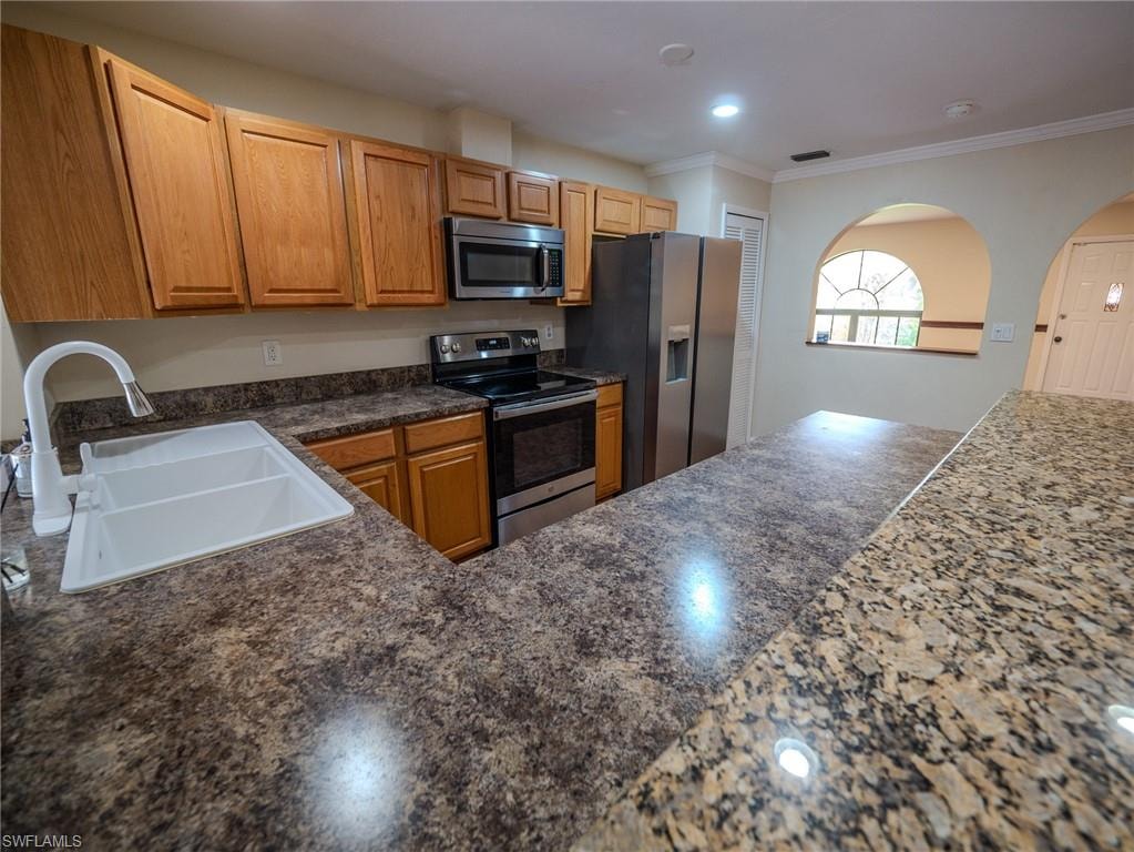 Kitchen featuring wood cabinetry, stainless steel appliances, a double basin sink with white faucet, and varied countertop finishes