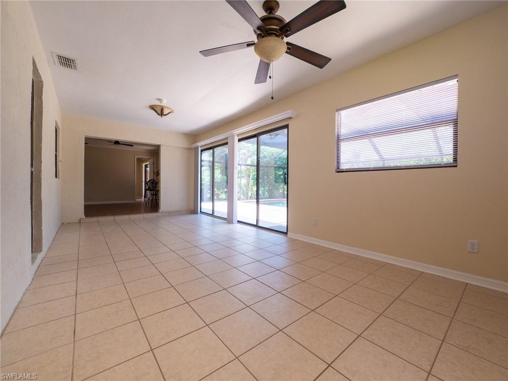 Spacious interior room featuring light-toned tile flooring, direct access to a patio area through sliding glass doors, a ceiling fan with integrated lighting, and a recessed window with horizontal blinds
