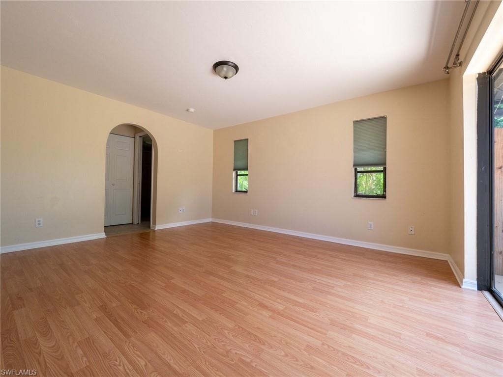 Spacious room featuring wood-finish flooring, an arched doorway, and multiple windows with roller shades