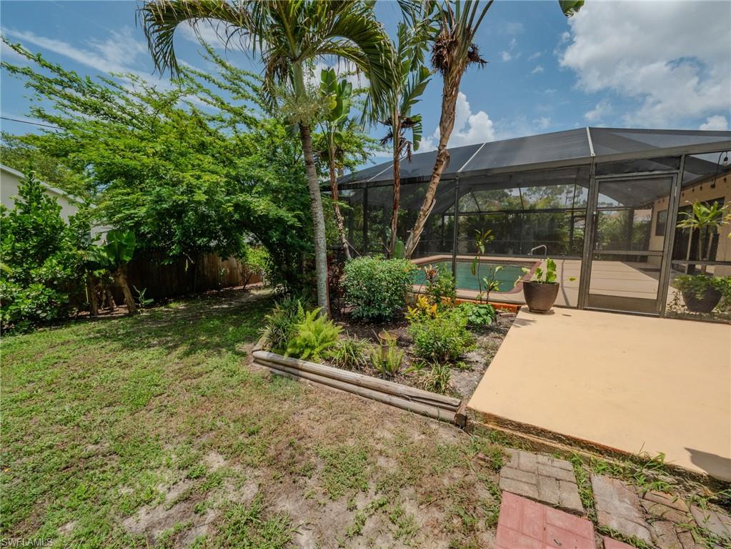 Screened outdoor swimming pool enclosure with a surrounding deck, complemented by a landscaped garden bed featuring palm trees and diverse plantings