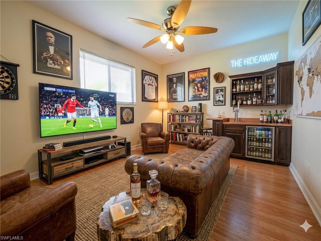Spacious entertainment area featuring wood-finish flooring, a built-in wet bar with cabinetry and beverage refrigerator, and a ceiling fan