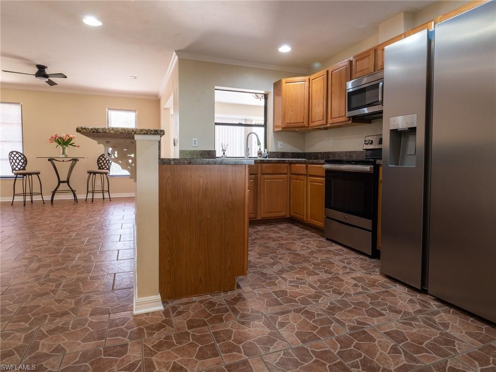 Kitchen featuring wood cabinetry, stainless steel appliances, dark countertops, and patterned tile flooring