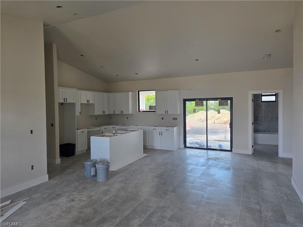 Spacious open-concept interior featuring light gray tile flooring, vaulted ceilings with recessed lighting, and white cabinetry