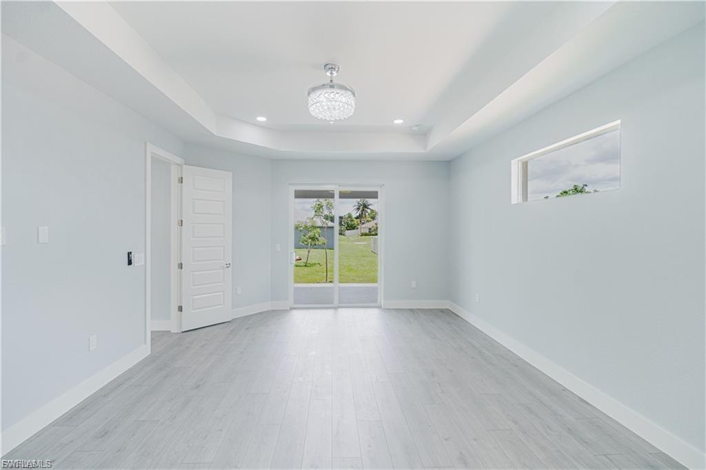 Spacious interior room featuring wood-finish flooring, tray ceiling with recessed lighting and a decorative chandelier, and sliding glass doors opening to the exterior