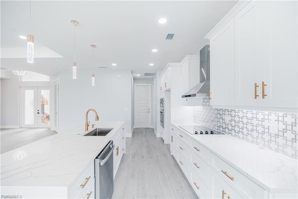 Modern kitchen featuring white cabinetry with gold-tone hardware, a large island with an integrated sink and dishwasher, and a patterned tile backsplash