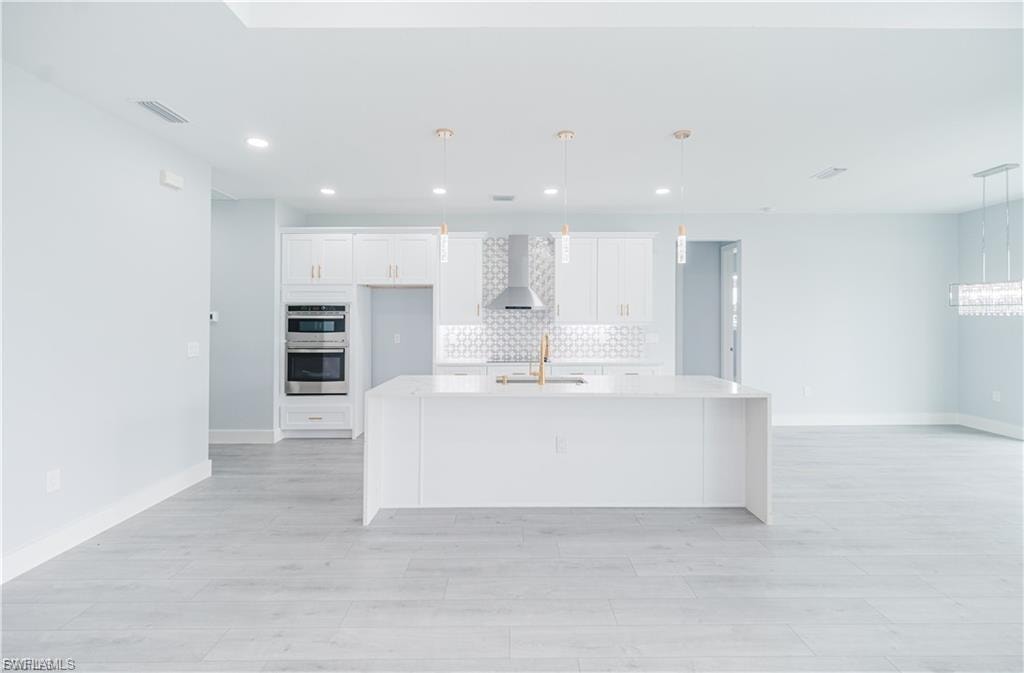 Open-concept kitchen featuring a white center island, coordinating cabinetry, stainless steel double wall ovens, and a decorative tile backsplash