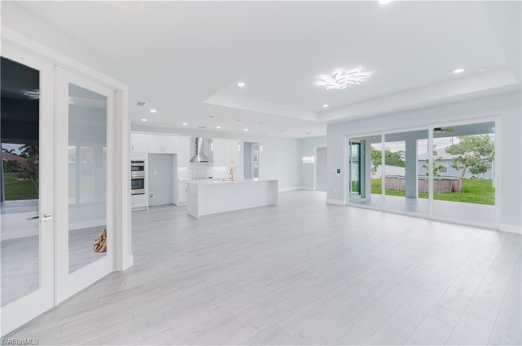 Open-concept living space featuring wood-finish flooring, recessed lighting, and a tray ceiling with a decorative fixture