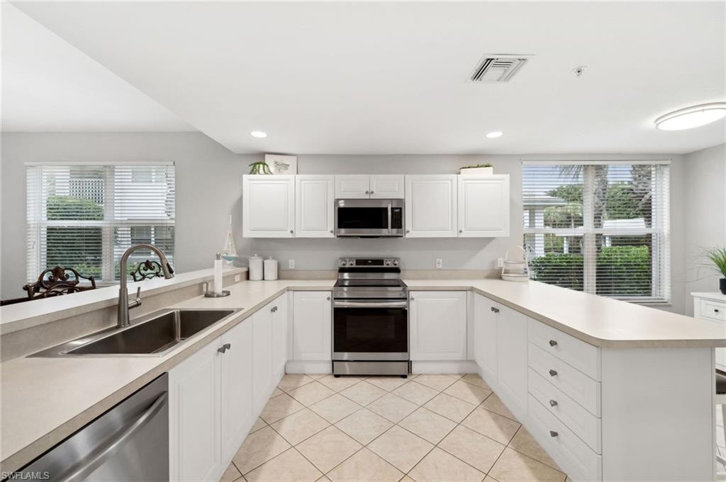 Kitchen with sink, appliances with stainless steel finishes, light tile patterned floors, and kitchen peninsula
