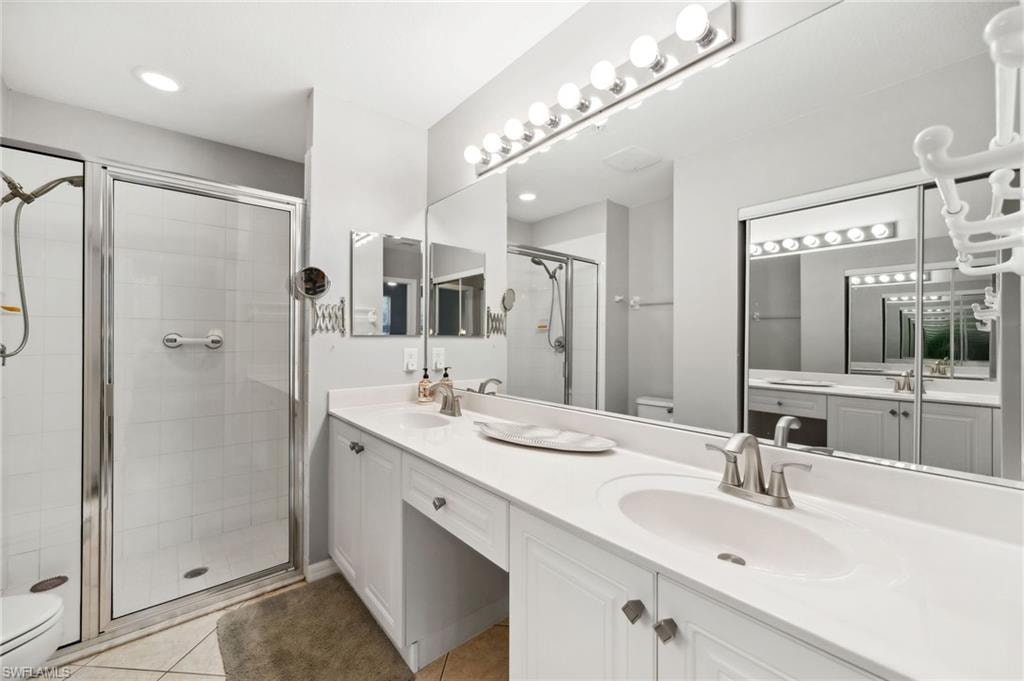 Bathroom with double vanity, tile patterned floors, a shower with shower door, and toilet