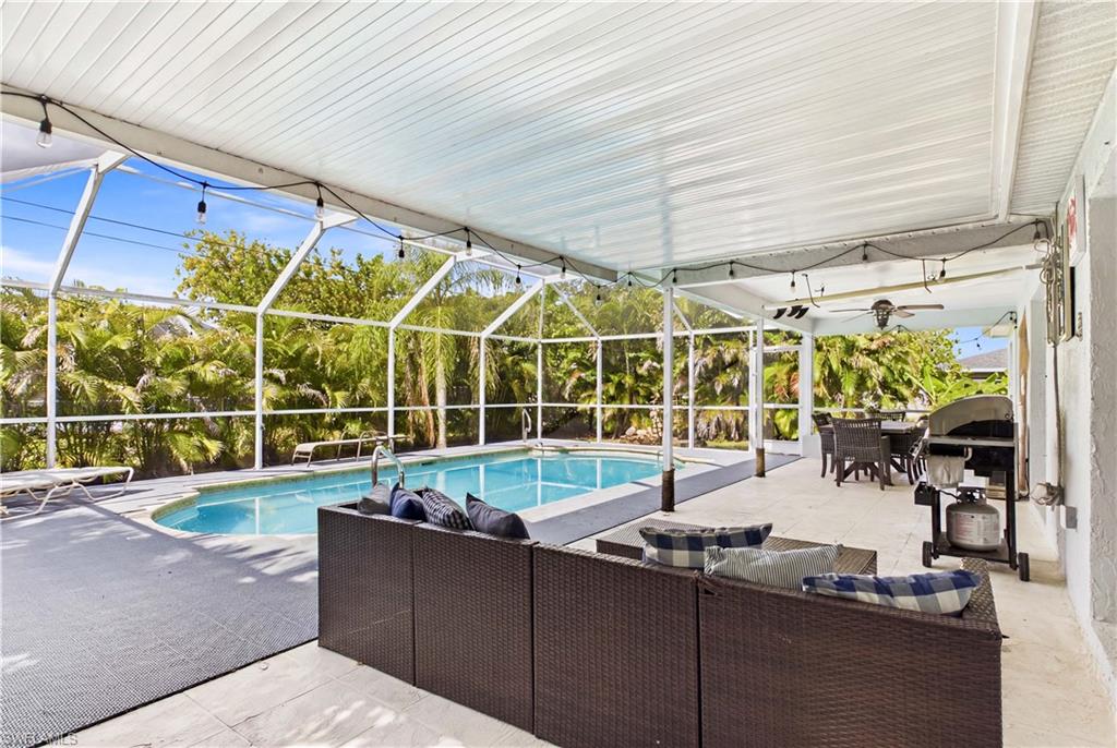 Screened pool enclosure featuring a curvilinear pool, ample patio space, a covered lanai, a ceiling fan, and string lighting