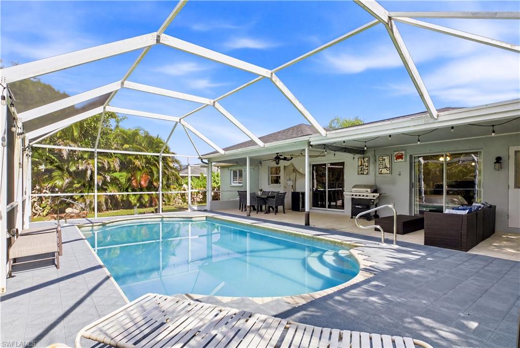 Screened pool enclosure featuring a curvilinear pool with integrated steps, a gray tile pool deck, and direct access to the interior via sliding glass doors