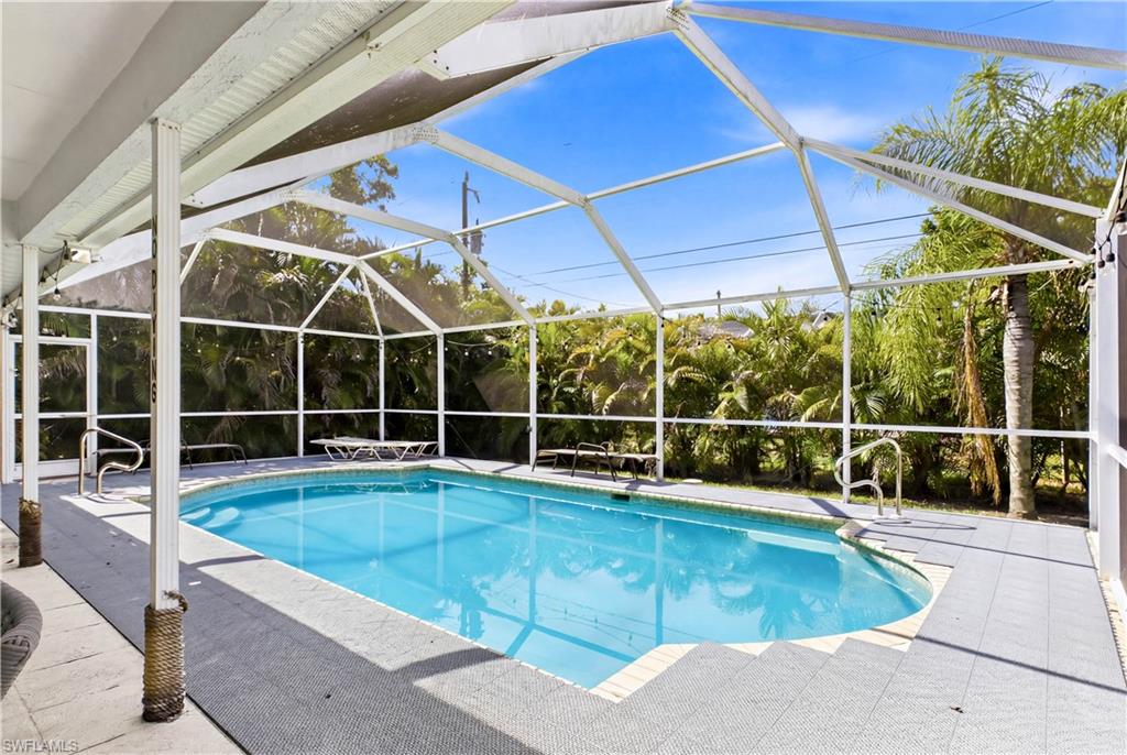 Screened swimming pool enclosure featuring an in-ground pool, surrounding gray tile patio, and tropical foliage