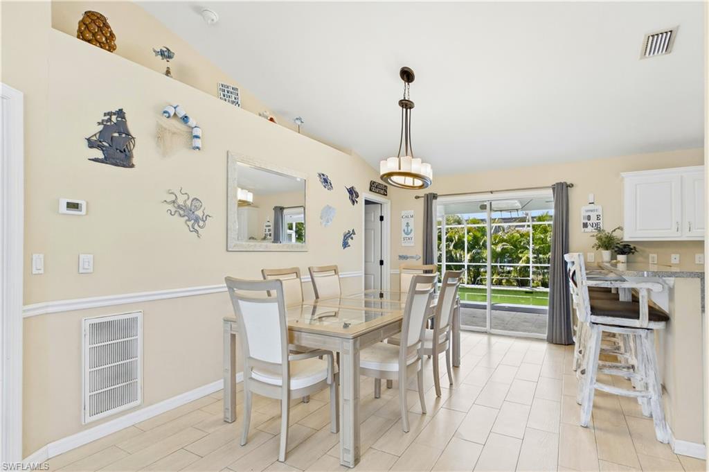 Open concept dining area with light-toned tile flooring, direct access to the outdoor area via sliding glass doors, a tray ceiling, and a built-in breakfast bar with white cabinetry