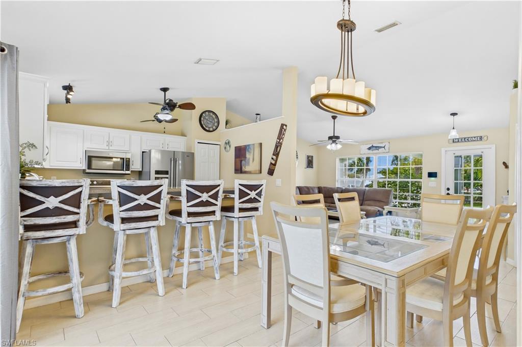 Open-concept living space featuring a dining area with a glass-top table, a kitchen island with seating for four, white cabinetry, and stainless steel appliances