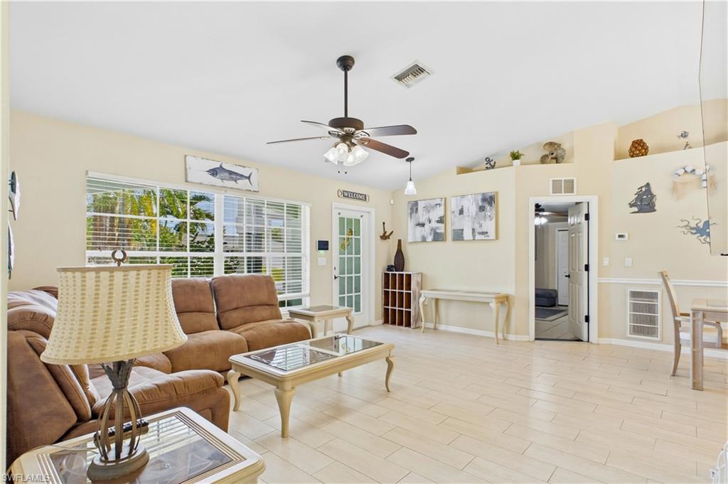 Spacious living area featuring light-toned tile flooring, vaulted ceilings, and a ceiling fan with light fixture