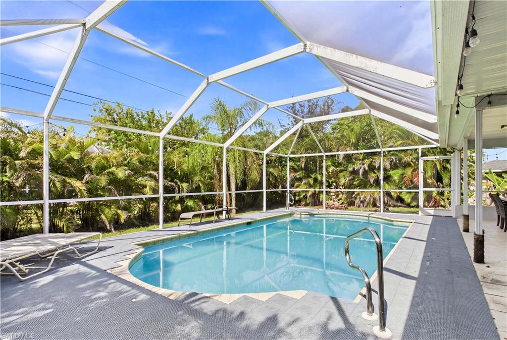 Screened pool enclosure featuring an inground swimming pool with curved edges, a metal handrail, and a concrete pool deck