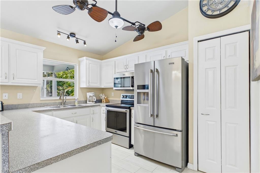 Bright kitchen featuring white cabinetry, light-toned countertops, stainless steel appliances, a double basin sink, and tile flooring