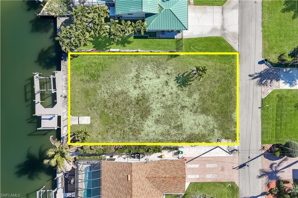 Waterfront lot featuring a concrete boat dock with multiple slips, a grass lawn, and mature palm trees - Virtually Edited Image