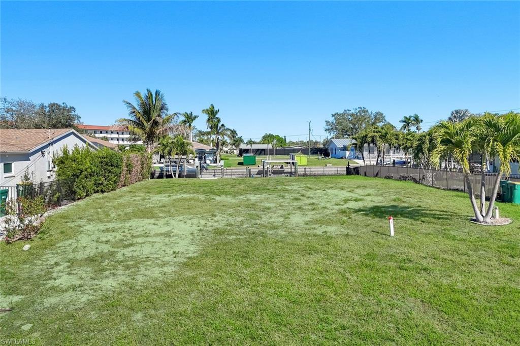 Expansive grass lot featuring mature palm trees and perimeter fencing - Virtually Edited Image