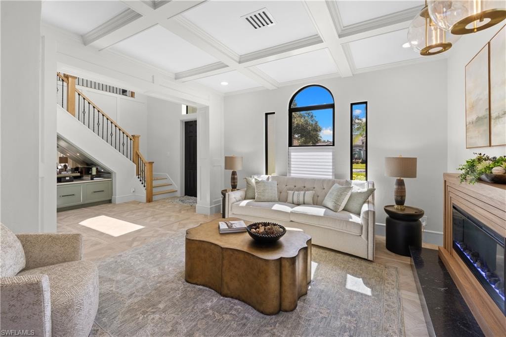 Living area featuring coffered ceilings, wood-finish flooring, a contemporary fireplace with a wood-paneled surround and black hearth, and an arched window with an additional vertical window