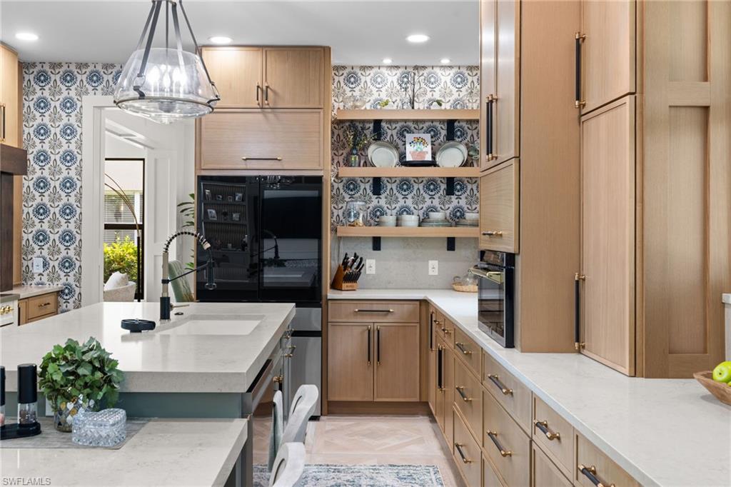 Open-concept kitchen featuring extensive light wood cabinetry, stone countertops, integrated appliances, and a central island with an undermount sink