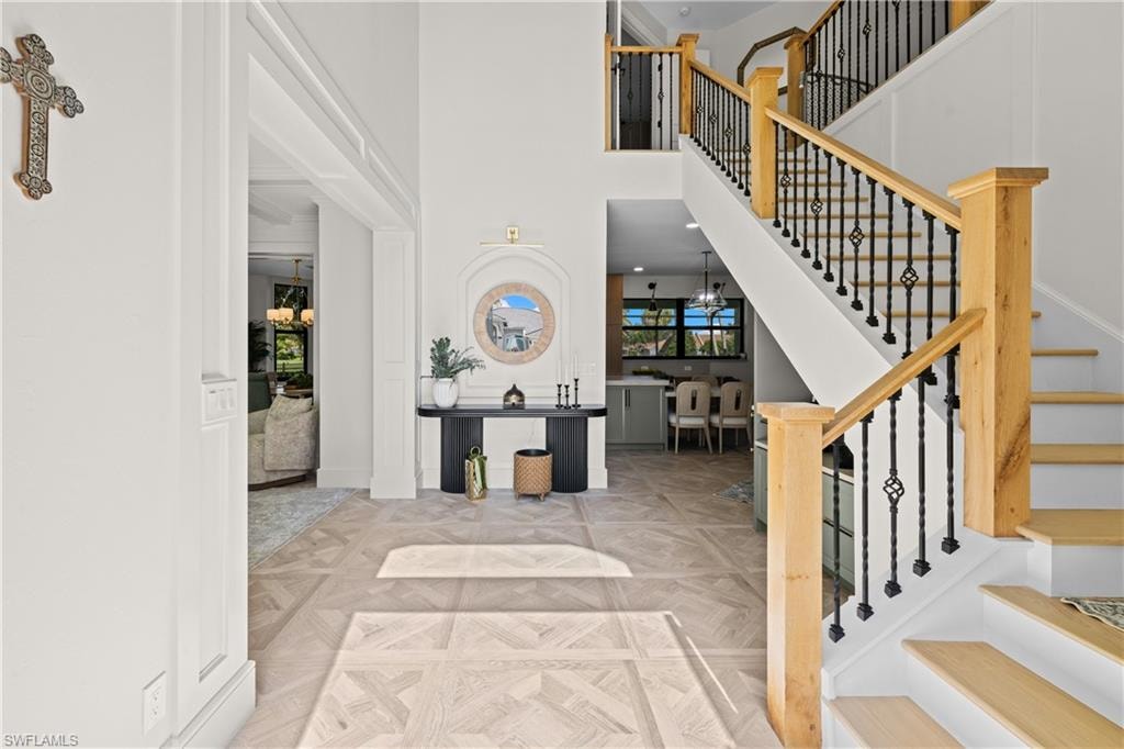 Grand entry foyer featuring light wood-finish flooring with a geometric pattern, a prominent staircase with wood handrails and wrought iron balusters, and high ceilings