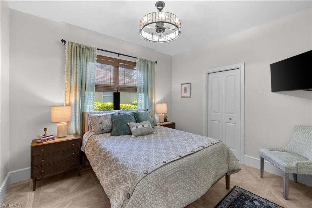 Bedroom featuring wood-finish herringbone flooring, a crystal-banded ceiling fan with integrated lighting, and a window with both woven wood shades and drapery
