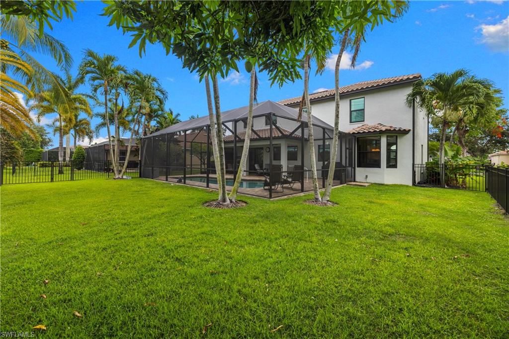 Expansive backyard featuring a screened-in pool enclosure, mature palm trees, a tiled roofline, and a black wrought iron fence