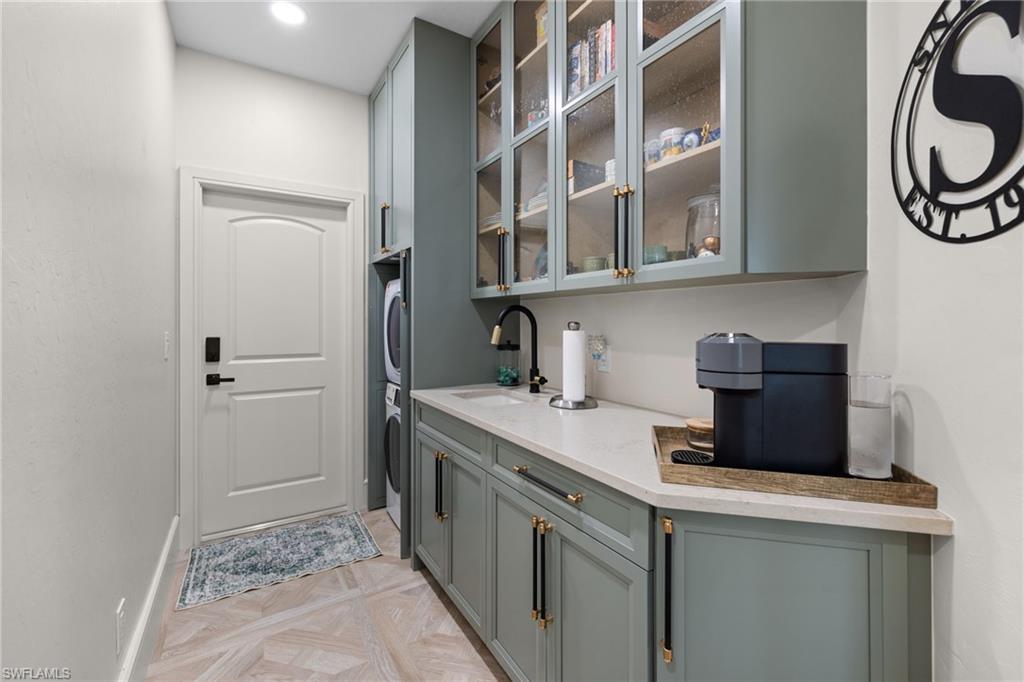 Dedicated utility space featuring stacked laundry appliances, light green cabinetry with gold-tone hardware, and a single-basin sink with a matte black faucet