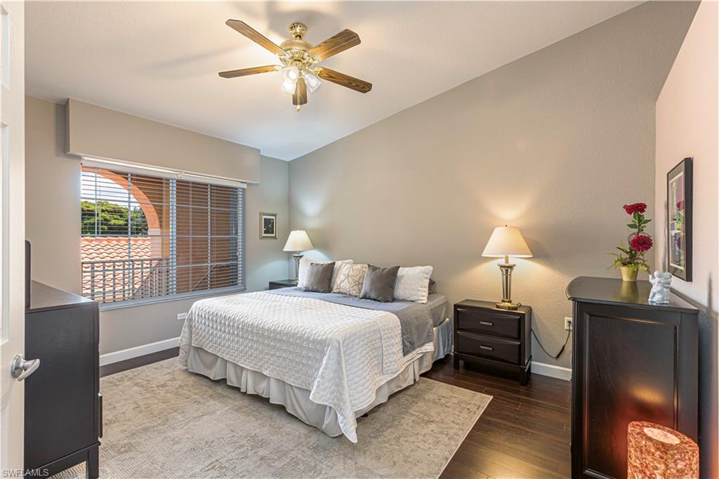 Vaulted ceiling bedroom with wood-finish flooring, a window with horizontal blinds, and a brass-finish ceiling fan