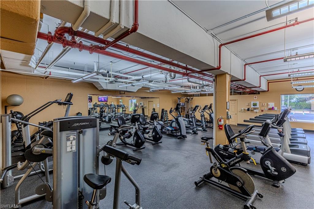Fitness center featuring extensive cardio equipment, strength training machines, mirrored walls, rubberized flooring, and exposed ceiling ductwork