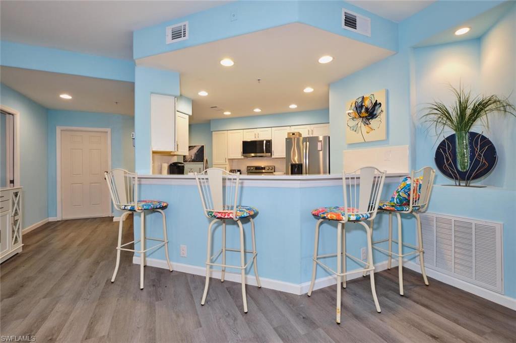 Kitchen with appliances with stainless steel finishes, wood finished floors, white cabinetry, a kitchen breakfast bar, and a peninsula