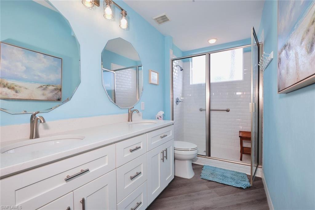 Bathroom featuring double vanity, a stall shower, and wood finished floors