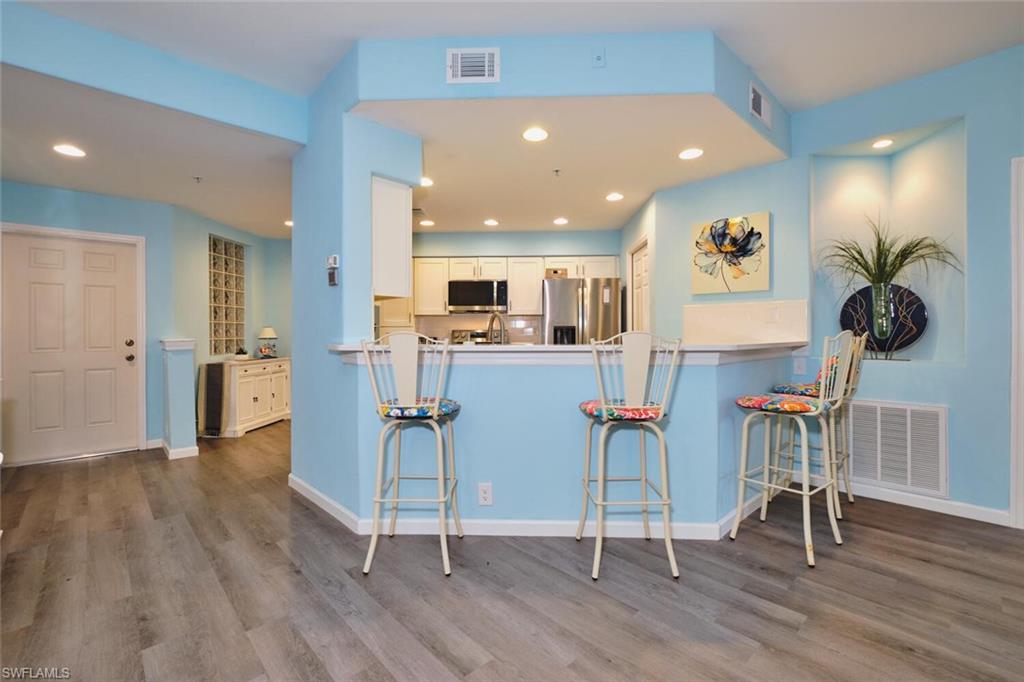 Kitchen with appliances with stainless steel finishes, wood finished floors, a peninsula, a kitchen breakfast bar, and recessed lighting