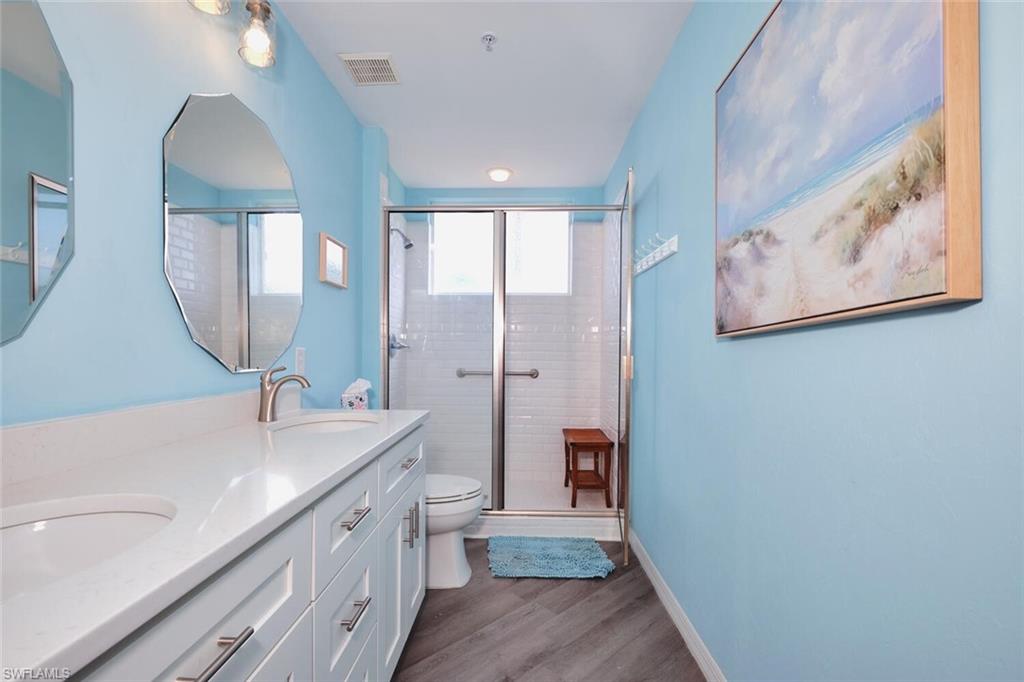 Bathroom with wood finished floors, double vanity, and a stall shower