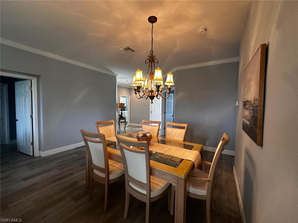 Dining area featuring dark wood finished floors, crown molding, and a chandelier