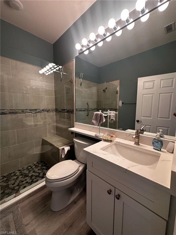 Bathroom featuring wood finished floors, vanity, and tiled shower