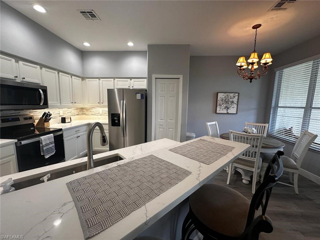 Kitchen featuring stainless steel appliances, a chandelier, white cabinetry, pendant lighting, and a breakfast bar area