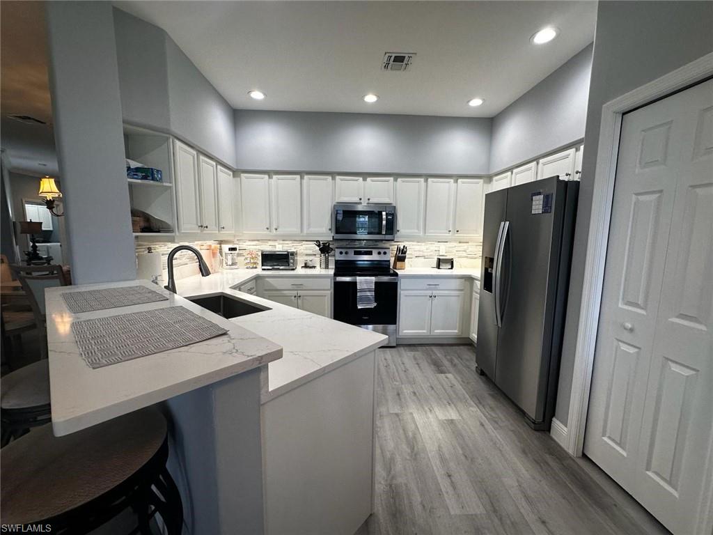 Kitchen with a peninsula, stainless steel appliances, light stone counters, open shelves, and backsplash