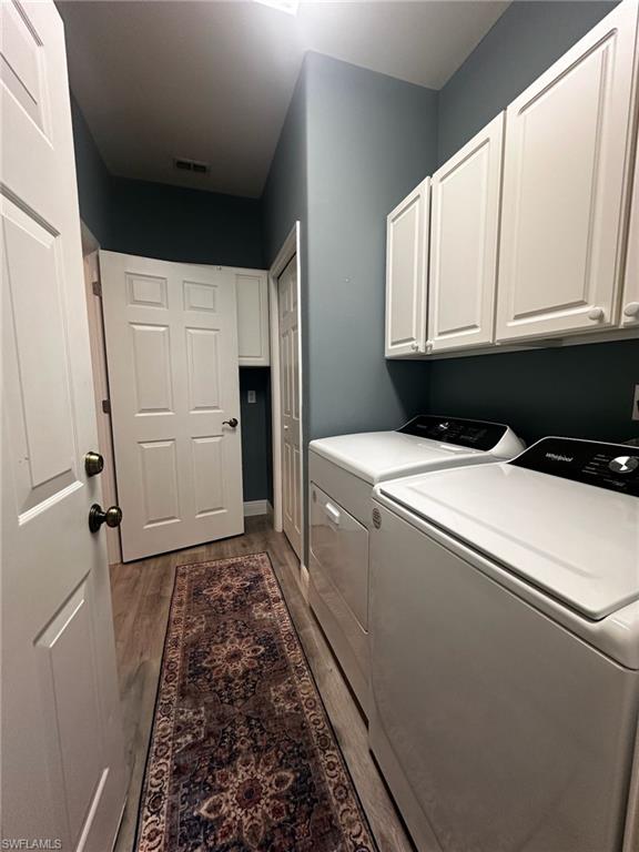 Washroom featuring washing machine and dryer, cabinet space, and wood finished floors