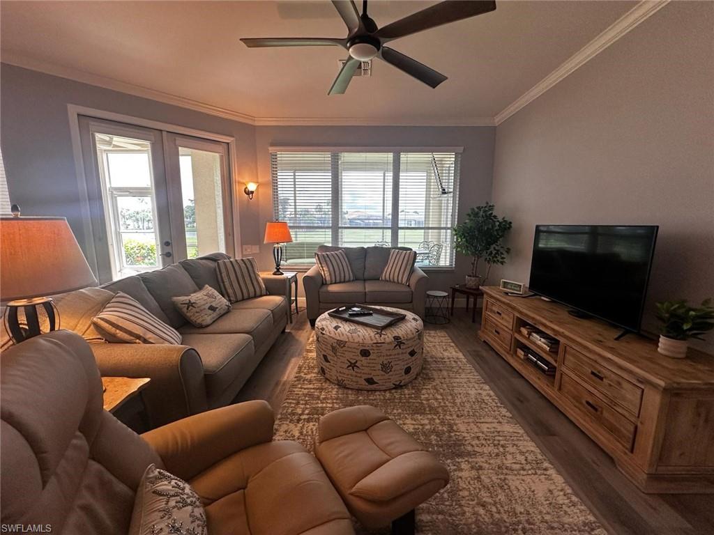 Living room with dark wood-style flooring, crown molding, ceiling fan, healthy amount of natural light, and french doors